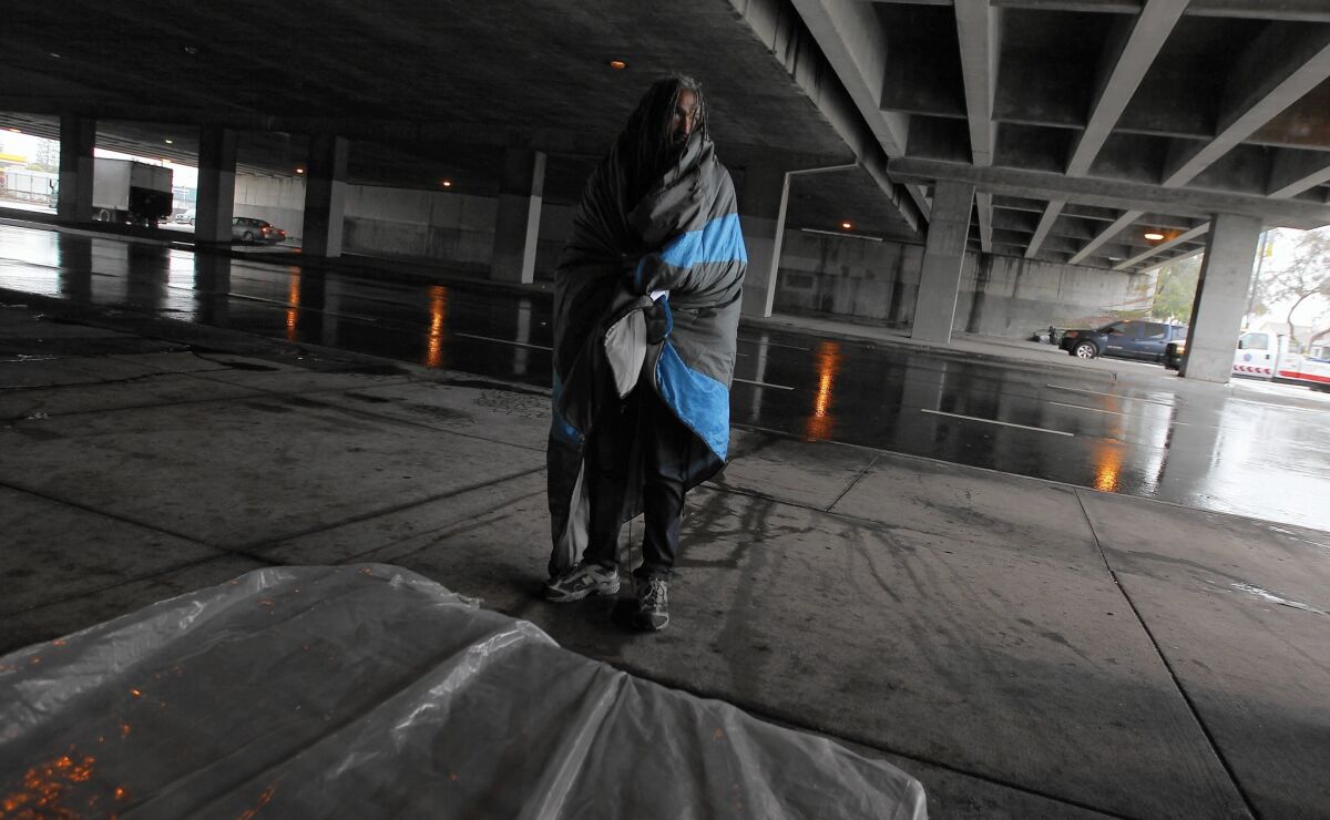 A homeless man who declined to be identified shelters beneath the 405 Freeway along Venice Boulevard as the rain comes down Tuesday.