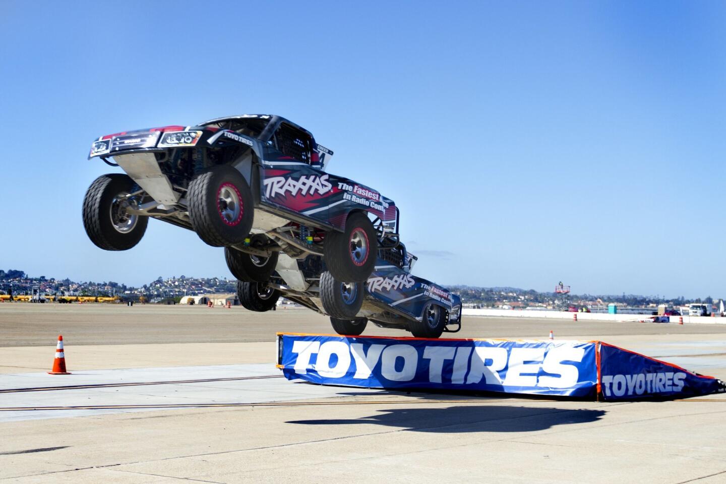 Two high-performance trucks cadapult off a ramp at high speeds.