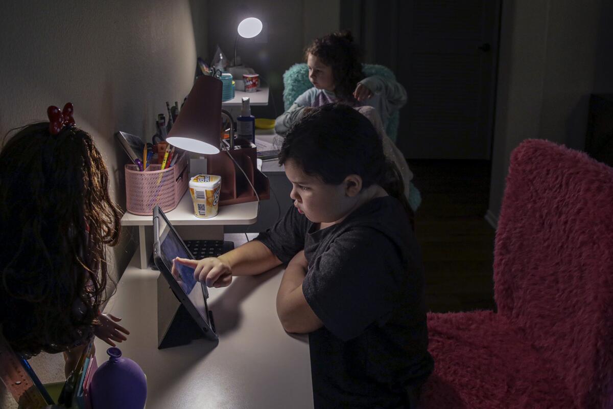 Two children sit at tables, looking at iPads.