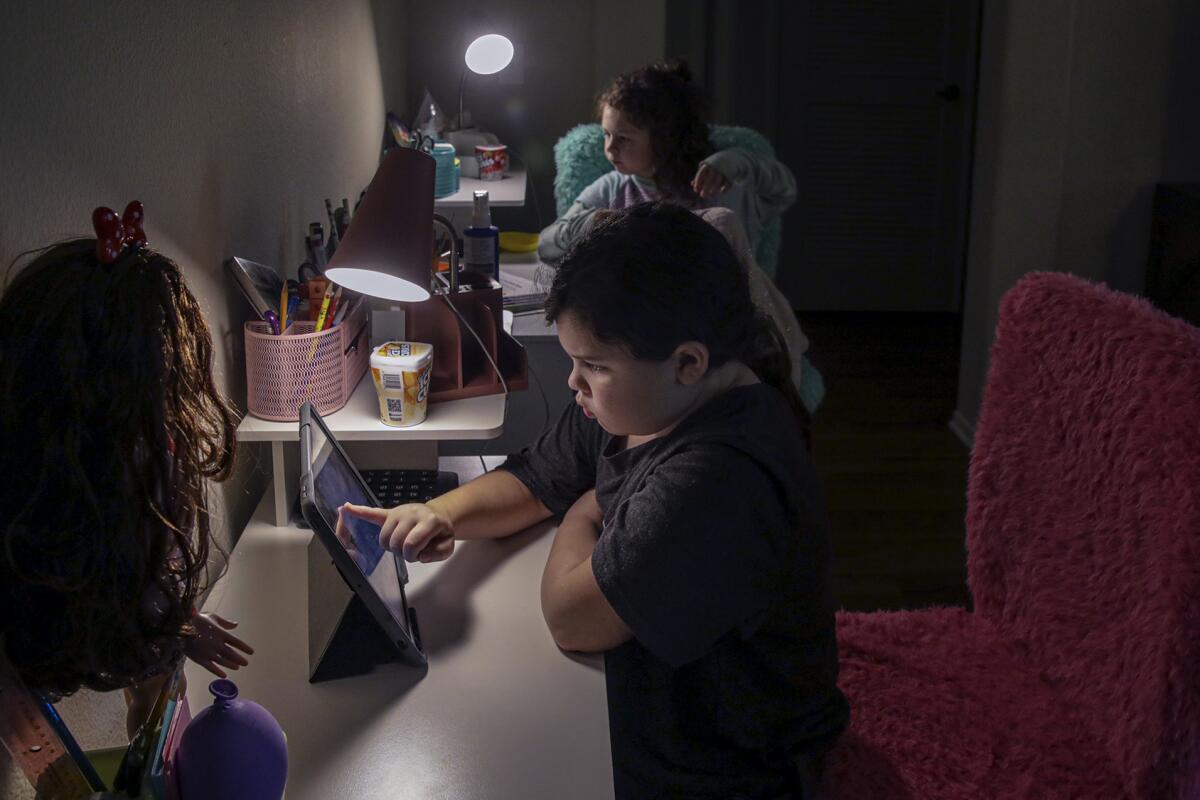 Two children sit at tables, looking at iPads. 