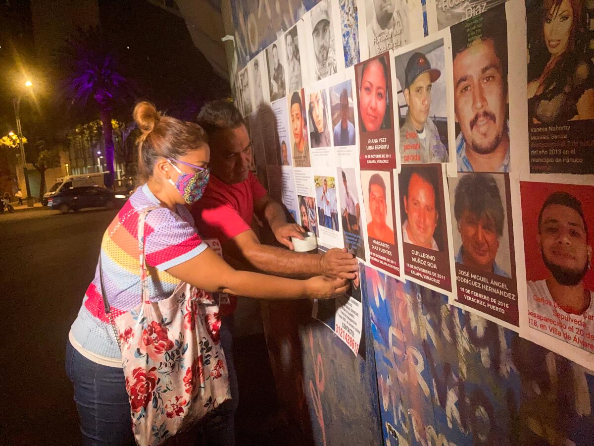 A woman and a man put up a poster alongside others on a wall 