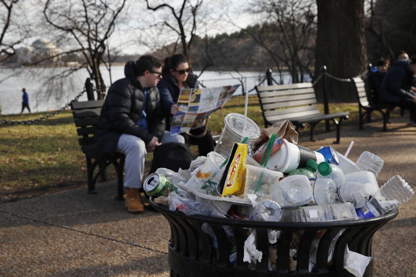 A trash can overflows with plastic waste at a park.