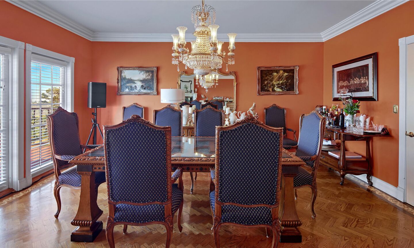 The dining room has orange walls and a dining table and chairs overlooking a window.