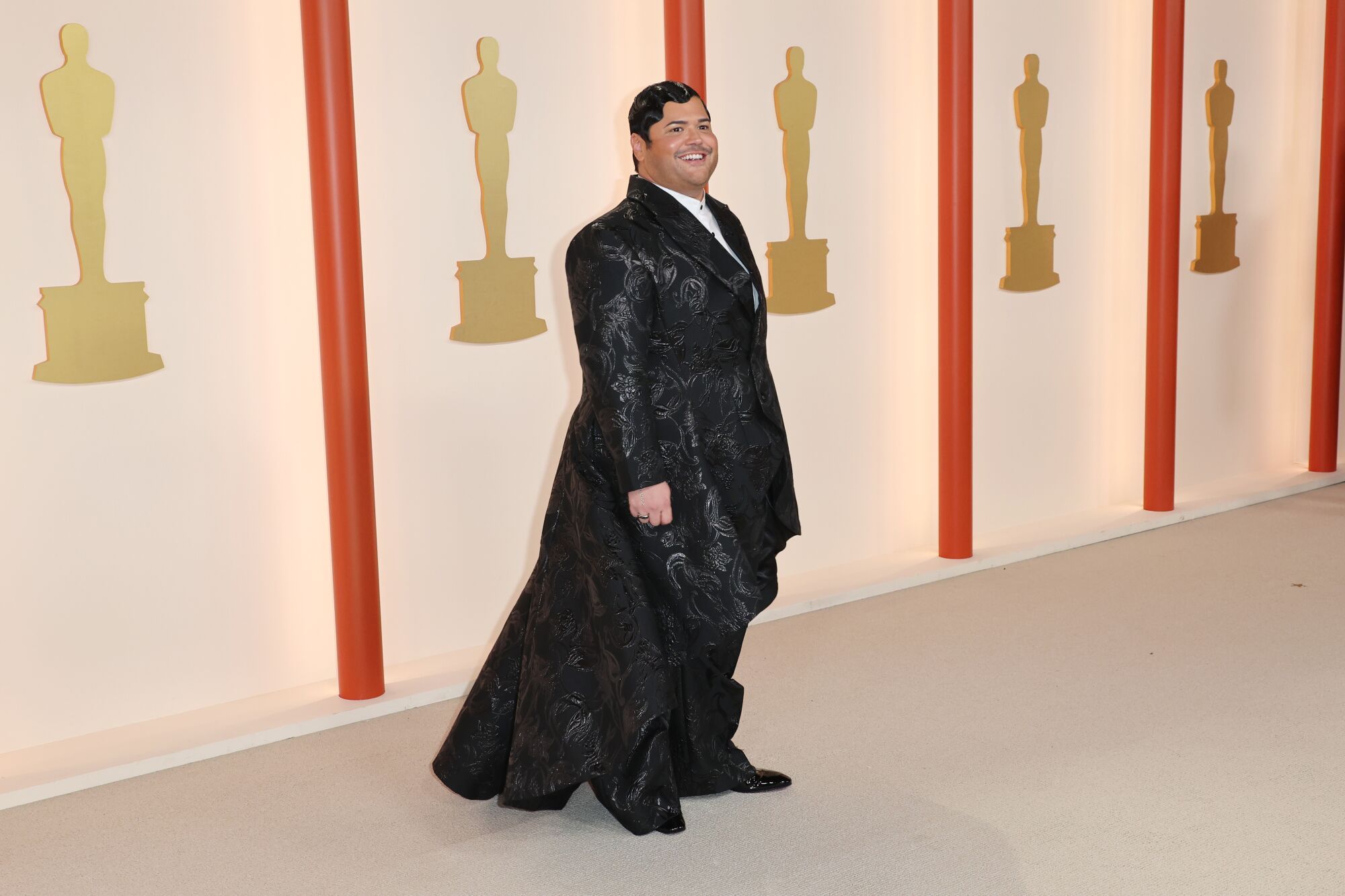 Harvey Guillén in a black tux with floor-length black train.