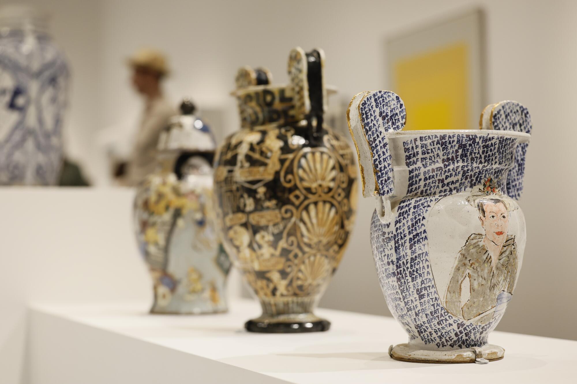 Vases, urns and other vessels painted sit atop white pedestals at a museum.