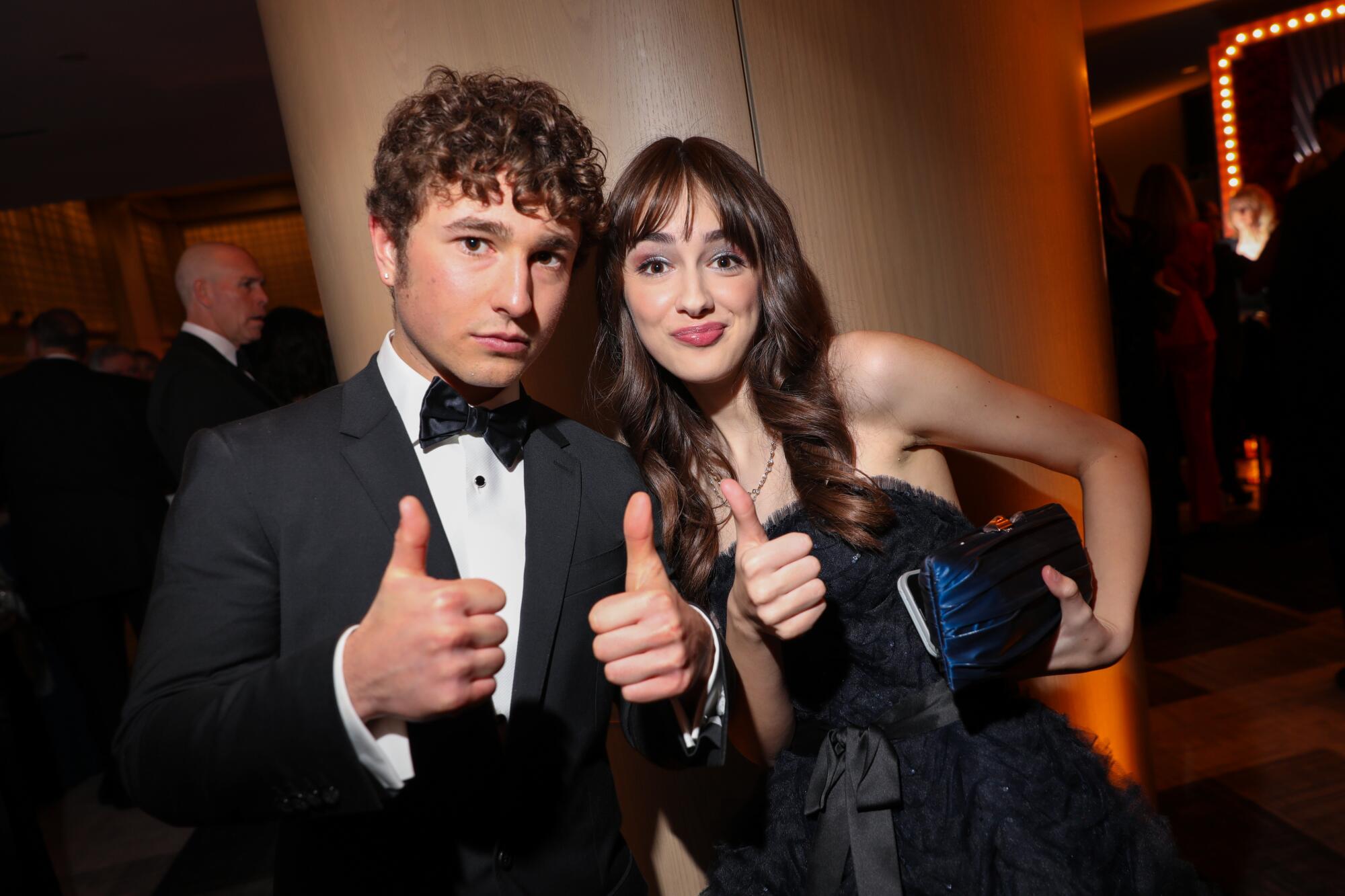 man in a tux and woman in a navy dress give thumbs up 