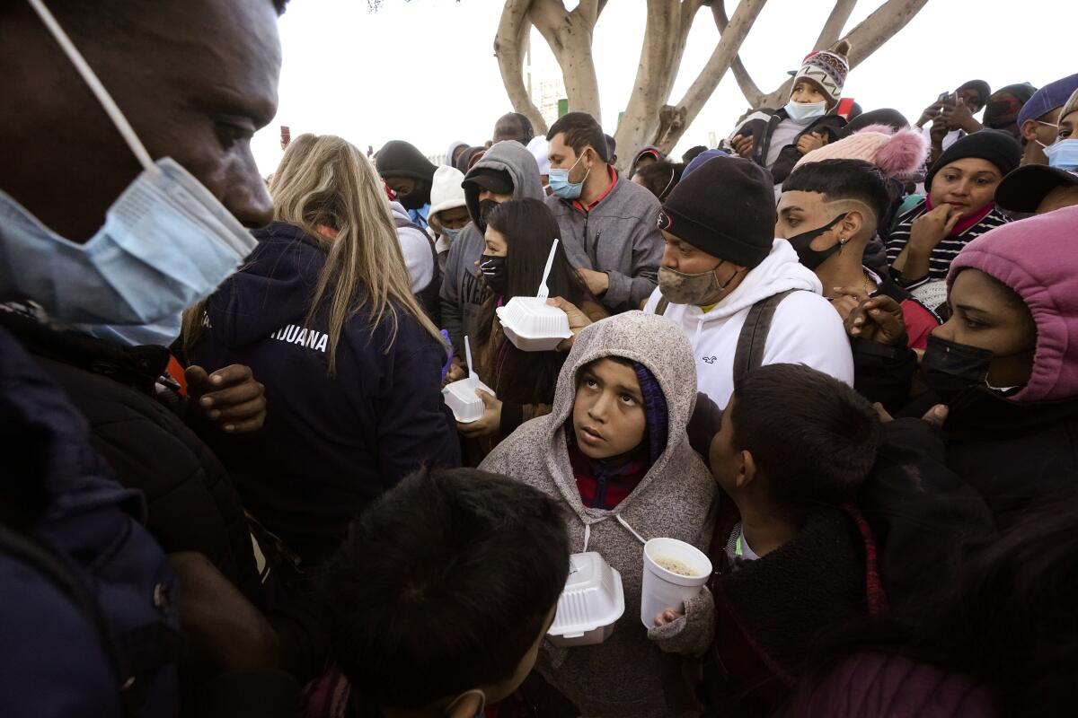 Amid a crowd, a child holds a styrofoam carton and cup with food.