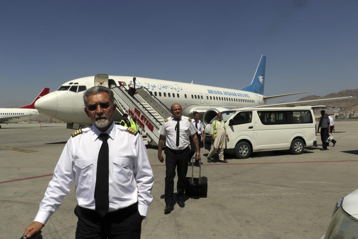 Pilots walk with suitcases with an airplane in the background.