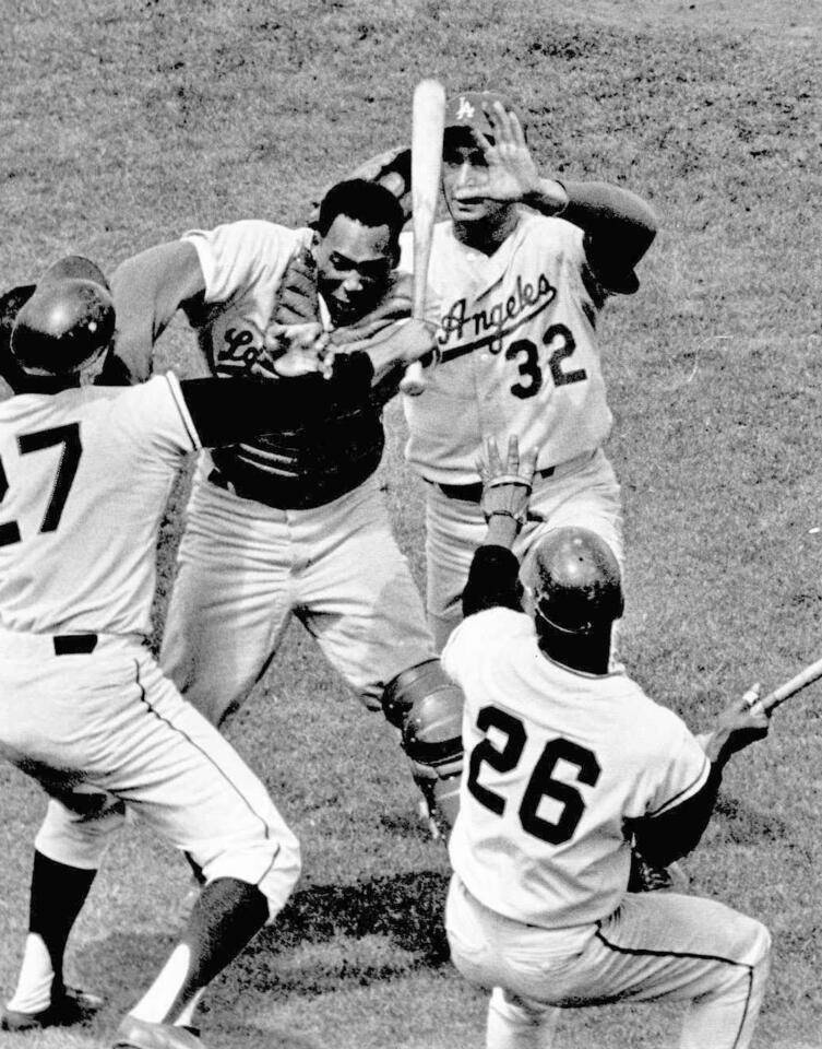 San Francisco pitcher Juan Marichal (27) swings a bat at Dodgers catcher John Roseboro (8) as Dodgers pitcher Sandy Koufax (32) tries to intervene.