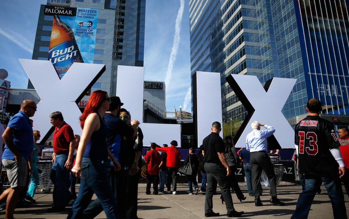 People walk past the logo for Super Bowl XLIX between the Seattle Seahawks and New England Patriots on Feb. 1 at University of Phoenix Stadium in Glendale, Ariz.