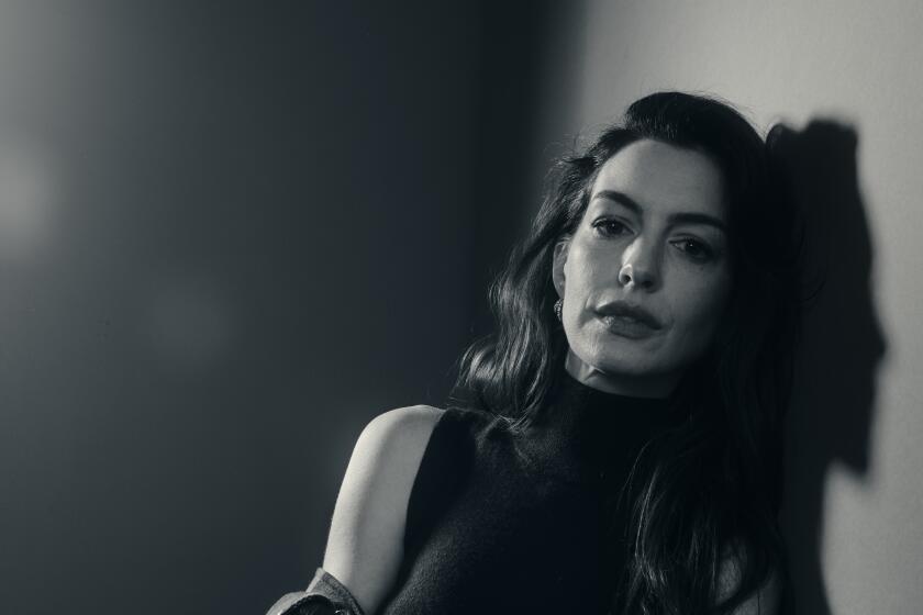 Anne Hathaway sits and leans against a wall in a black-and-white portrait