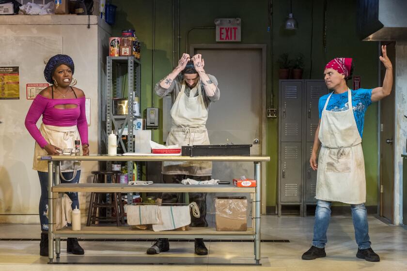 Three sandwich shop workers talk animatedly in a dingy commercial kitchen in a scene from "Clyde's" at the Mark Taper Forum.