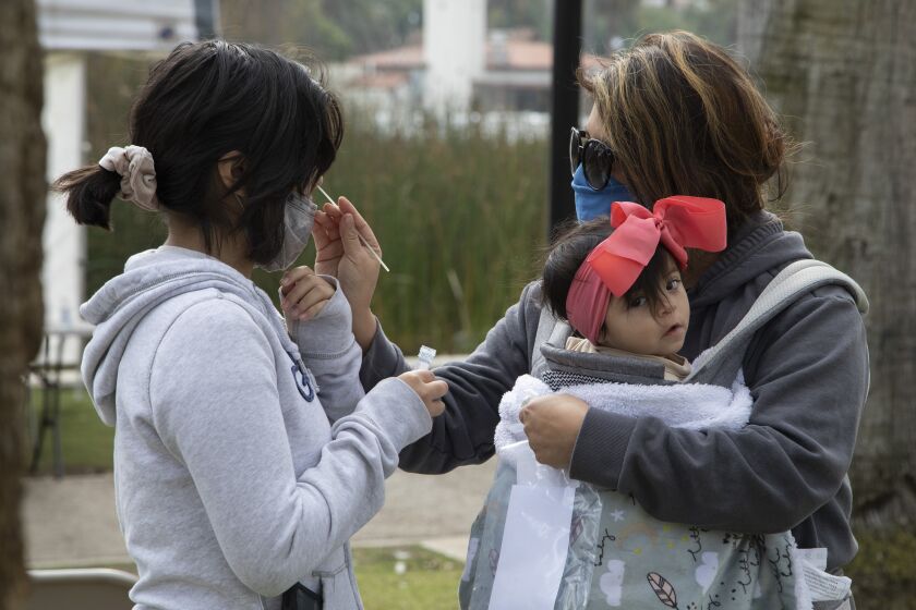LOS ANGELES, CA - JANUARY 18: Veronica Francisco, right, holding 9-month-old Alayla, swabs her daughter Abigail Campos, 11, during free COVID-19 testing at Echo Park on Tuesday, Jan. 18, 2022. The site was moved from Reservoir Street to provide a ``more convenient user experience'' amid a surge in COVID-19 cases related to the Omicron variant, Councilman Mitch O'Farrell said in an email to constituents Saturday. (Myung J. Chun / Los Angeles Times)