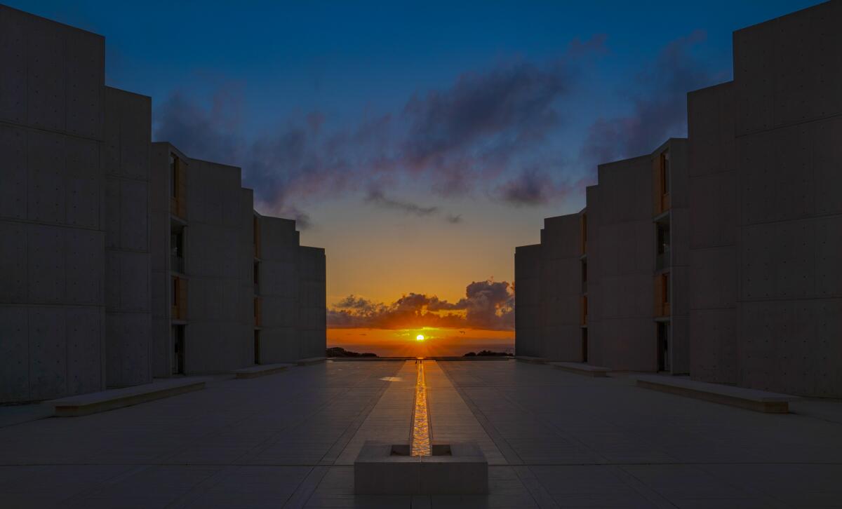 The setting sun lines up with a building's water feature.