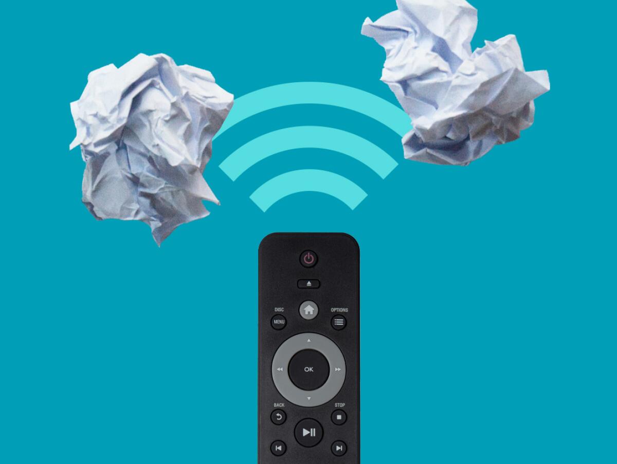 A remote control points toward two crumpled wads of paper.