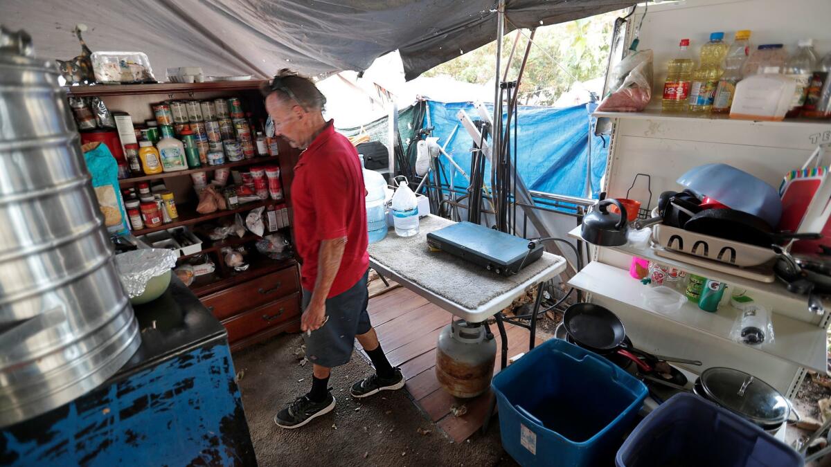 Scott West, 55, who has been homeless for five years, opens his pantry inside his tent compound along the Santa Ana River Trail next to Anaheim Stadium.