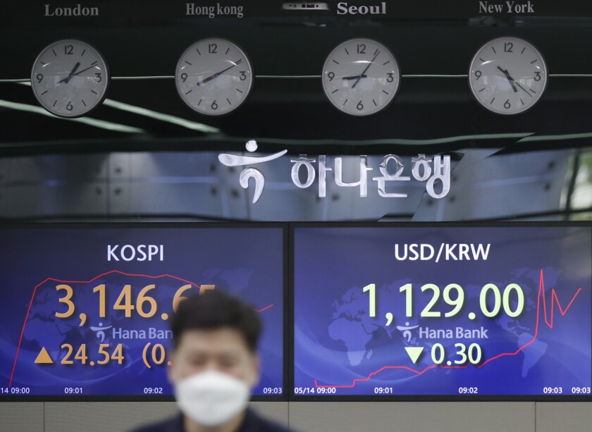 An employee of a bank walks by screens showing the Korea Composite Stock Price Index (KOSPI), left, and the foreign exchange rate between U.S. dollar and South Korean won at the foreign exchange dealing room in Seoul, South Korea, Friday, May 14, 2021. Asian shares rose Friday after Wall Street put the brakes on a three-day losing streak with a broad stock market rally powered by Big Tech companies and banks. (AP Photo/Lee Jin-man)