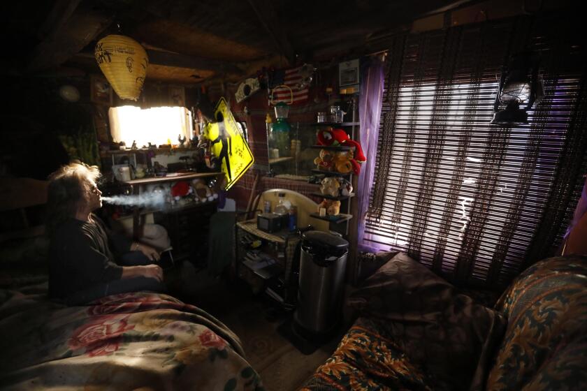 LANCASTER, CA - NOVEMBER 27, 2018 - - Steve Novak, 52, enjoys a smoke in the small cabin he constructed in the middle of a desert in Lancaster on November 27, 2018. He used to live in the cabin but now prefers to live in his RV parked nearby. Novak, originally from Woodland Hills, is a professional drummer and used to play with the group Fatal Thrust. Novak, who recently had a string of heart attacks, refers to his homeless community as, "Camp Coolness." ?If you?re at a hobo camp this is the coolest one you?ll ever see,? he said while sitting in his little house, which he made without the assistance of power tools. (Genaro Molina/Los Angeles Times)