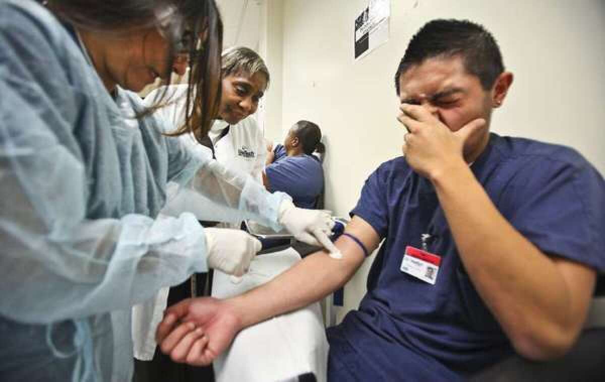 Student Daniel Morales, right, winces as a classmate takes a blood sample in a medical assistant class at WyoTech in Long Beach. WyoTech is one of 113 campuses run by Santa Ana-based Corinthian Colleges.