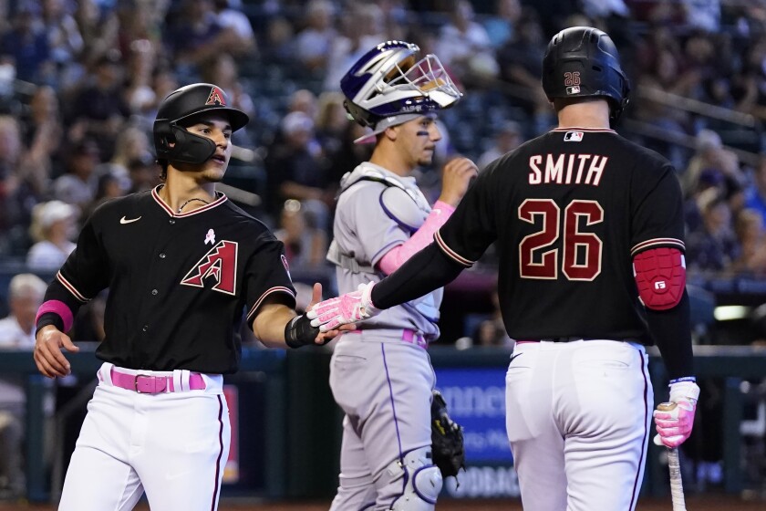 Arizona Diamondbacks' Alek Thomas, left, celebrates with teammate Pavin Smith (26) after scoring as Colorado Rockies catcher Dom Nunez, center, pauses at home plate in the fifth inning of a baseball game Sunday, May 8, 2022, in Phoenix. (AP Photo/Ross D. Franklin)