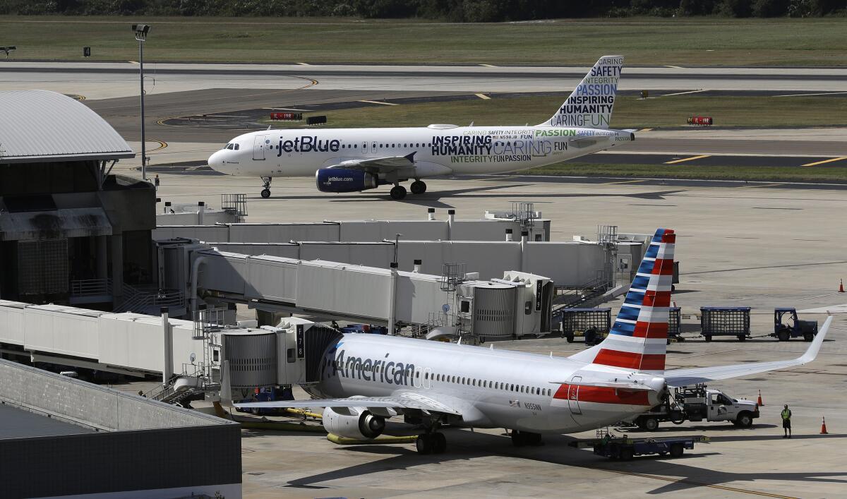 An American Airlines jet is seen parked at its gate as a JetBlue plane is in the background.
