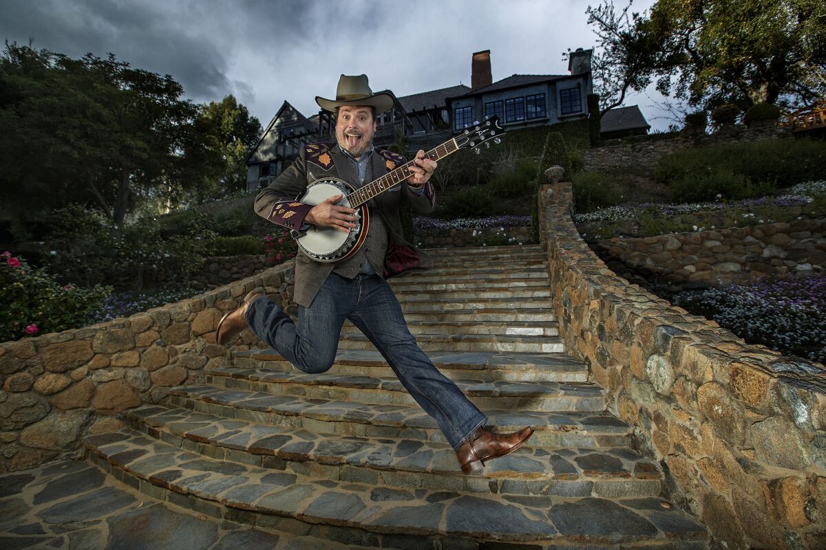 Jared Gutstadt, in front of Audio Up's compound, leaps in the air while playing a banjo. 