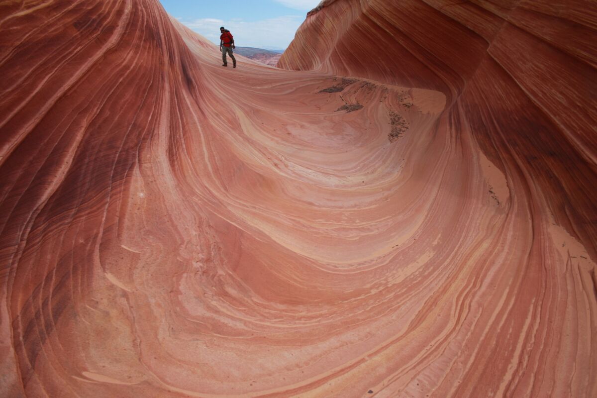 A hiker walks on a rock formation known as The Wave in the Vermilion Cliffs National Monument on the Utah-Arizona border.
