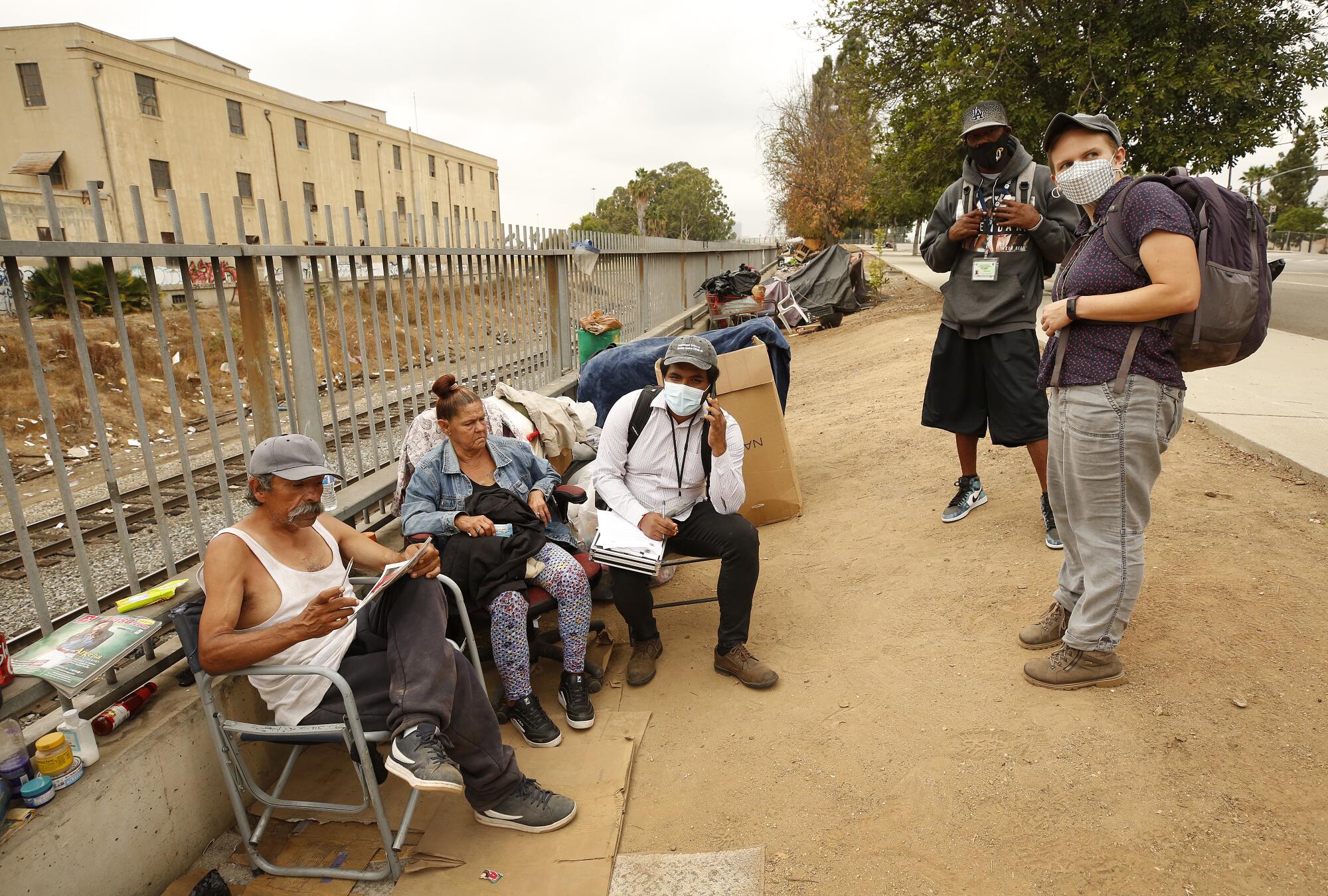 Outreach workers visit a couple seated next to train tracks.