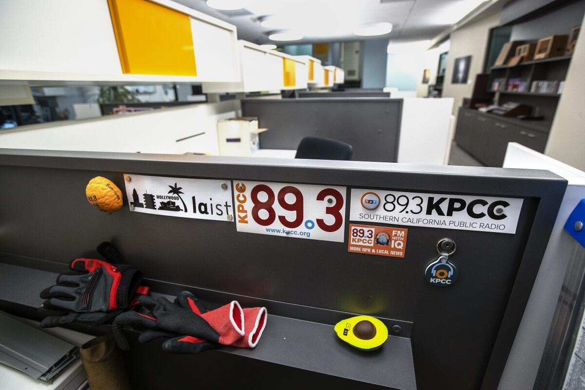 A cubicle desk in an office, adorned with 89.3 KPCC and LAist stickers, magnets, red gloves and an avocado toy.