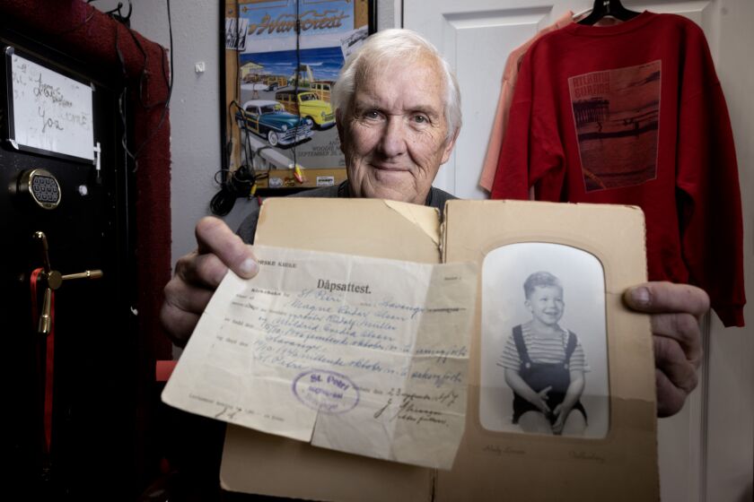 OCEANSIDE, CA - DECEMBER 27, 2022: Cardiff resident John Gundersen, 77, holds a photo of himself as a young boy and his original birth certificate while in his office at his business, called Woody Resin Surf Products, in Oceanside on Tuesday, December 27, 2022. In 2010, Gundersen discovered he was born through the Nazi Party's Lebensborn program, where young Norwegian women were encouraged to get impregnated by occupying Nazi soldiers to create thousands of Aryan babies during World War II. (Hayne Palmour IV / For The San Diego Union-Tribune)