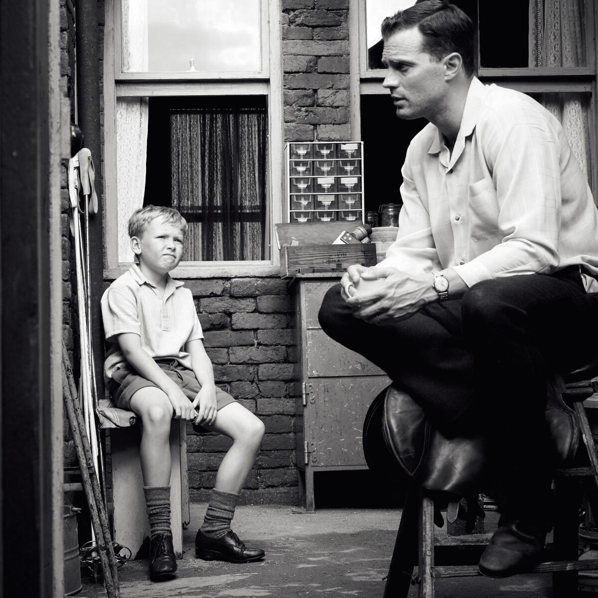 A black-and-white movie still shows a boy and his father sitting and talking.