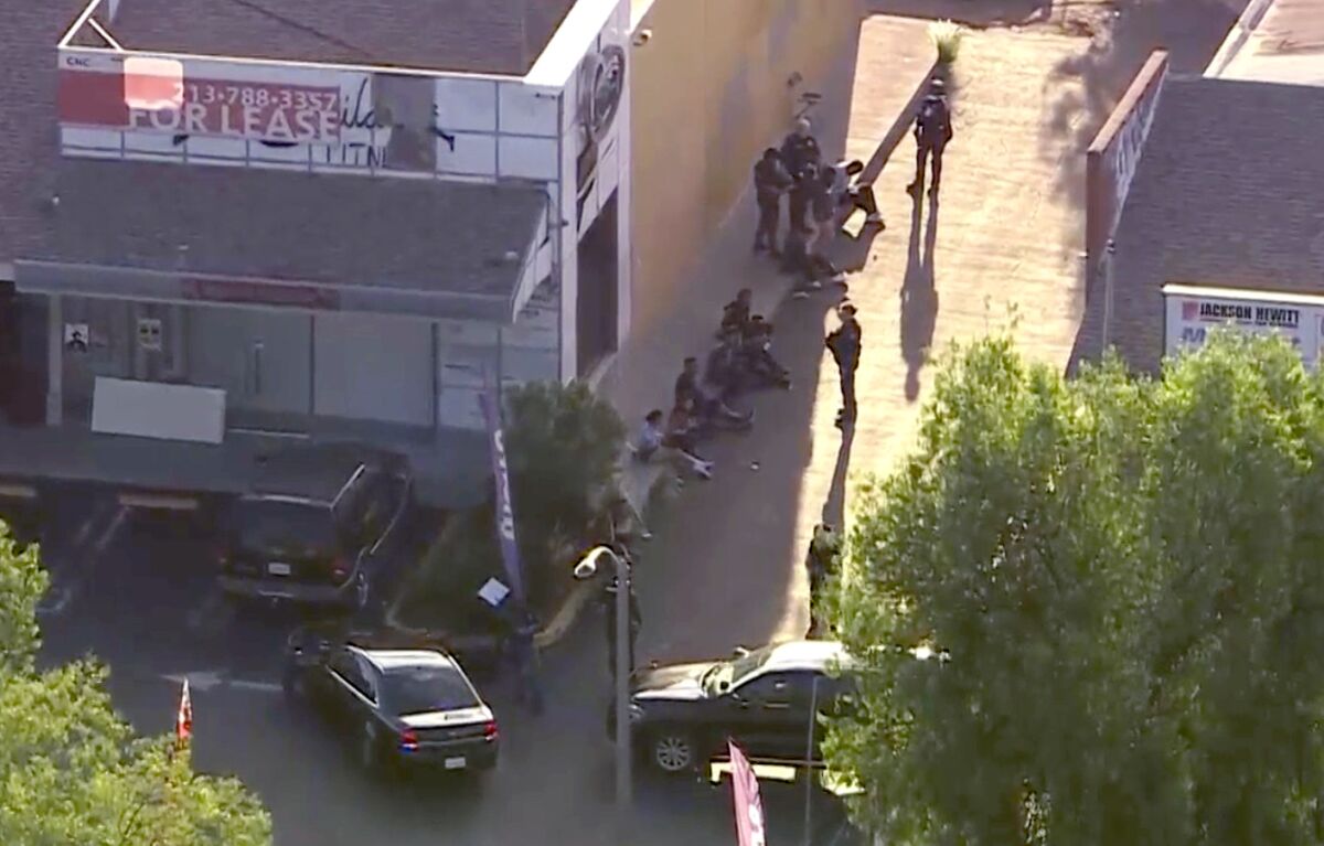 In an aerial image, people sit on pavement outside a building.