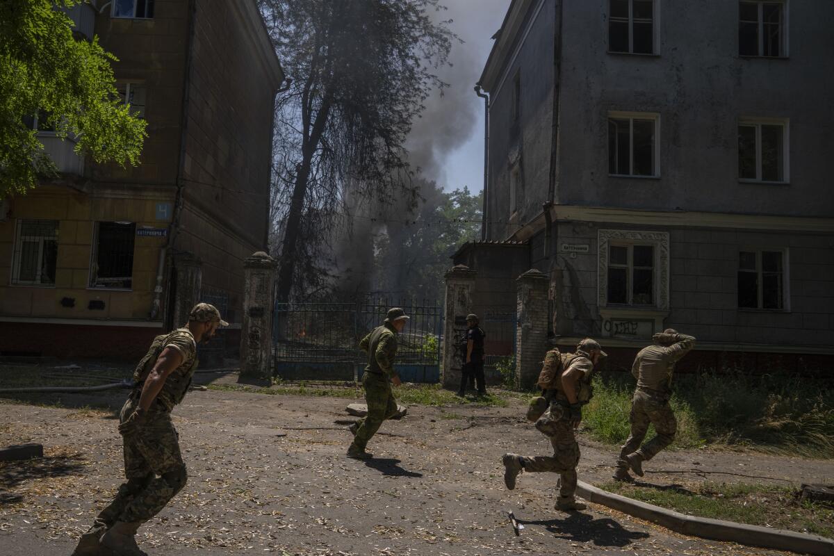 Ukrainian soldiers run across a street as smoke rises nearby