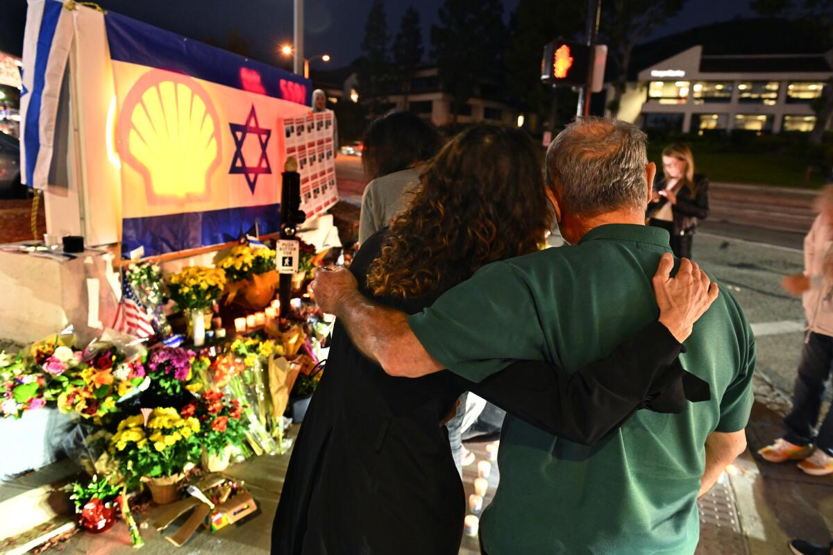 Two people embrace by a memorial at Shell gas station
