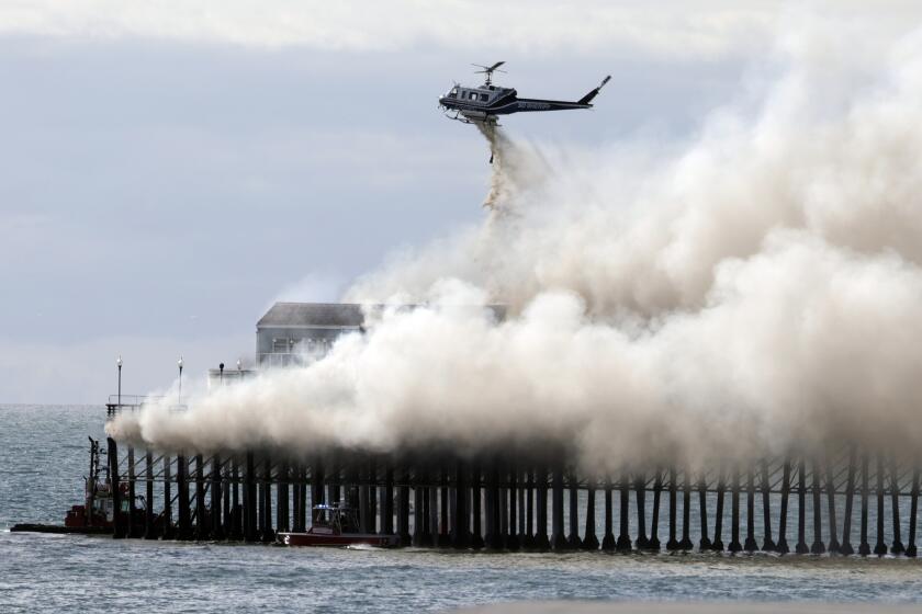 OCEANSIDE, CA - APRIL 25, 2024: A helicopter drops water as fire crews fight a fire burning at the end of the Oceanside Municipal Pier in Oceanside on Thursday, April 25, 2024.