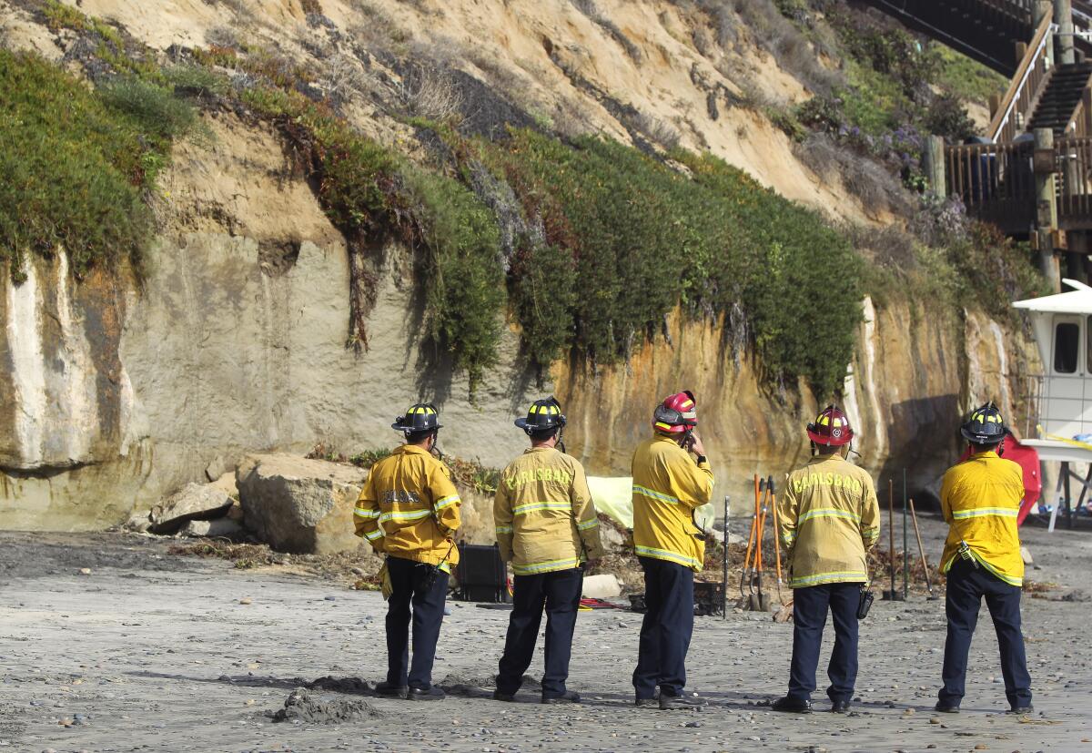 Firefighters look at a section of oceanfront bluff that collapsed Friday, killing three women.