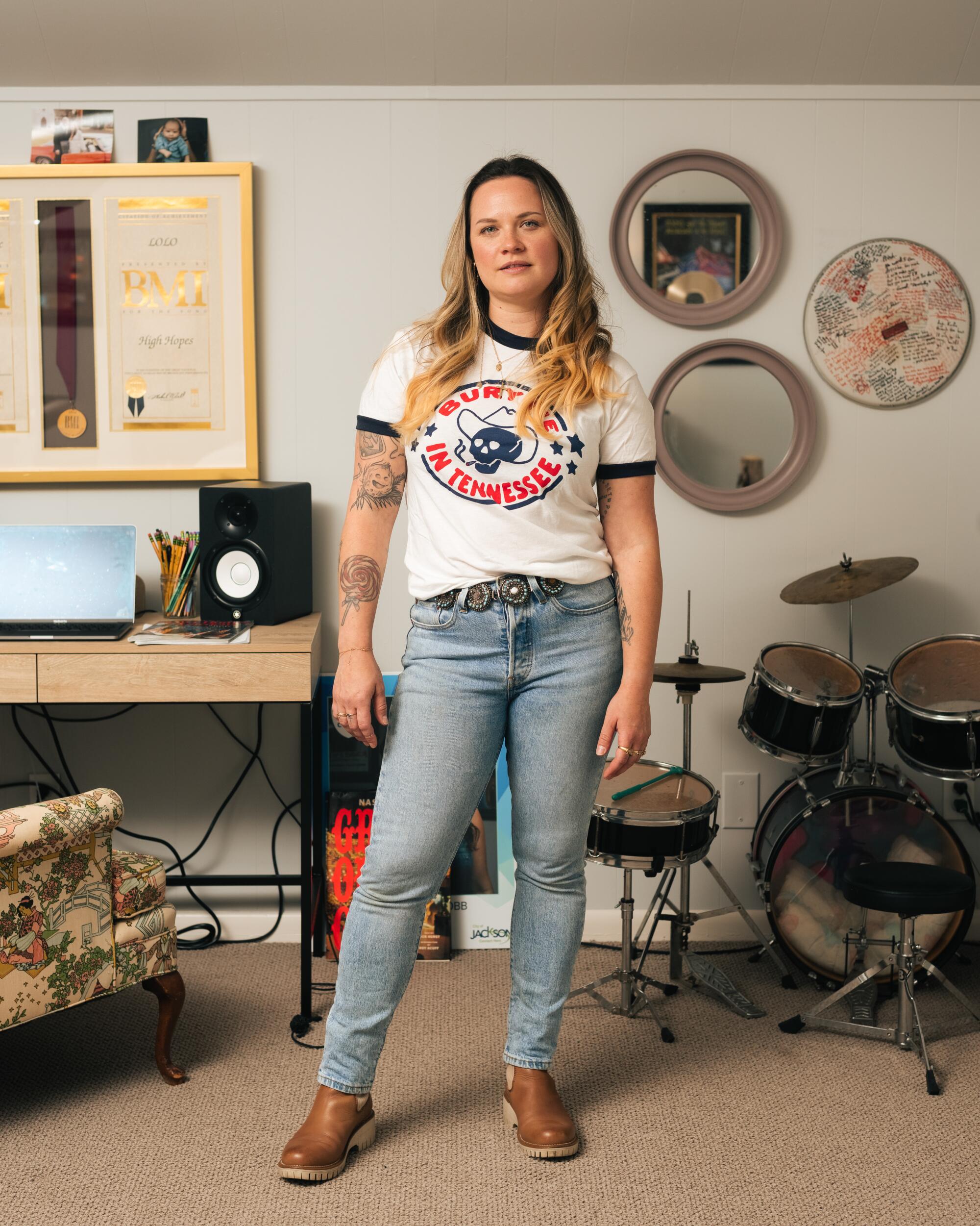 A woman wearing a "Bury Me in Tennessee" shirt stands in front of a set of drums.