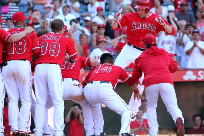 Angels designated hitter Mark Trumbo arrives at home plate with a leap into awaiting teammates after hitting the game-winning home run against the Tigers in the 13th inning Sunday afternoon in Anaheim.