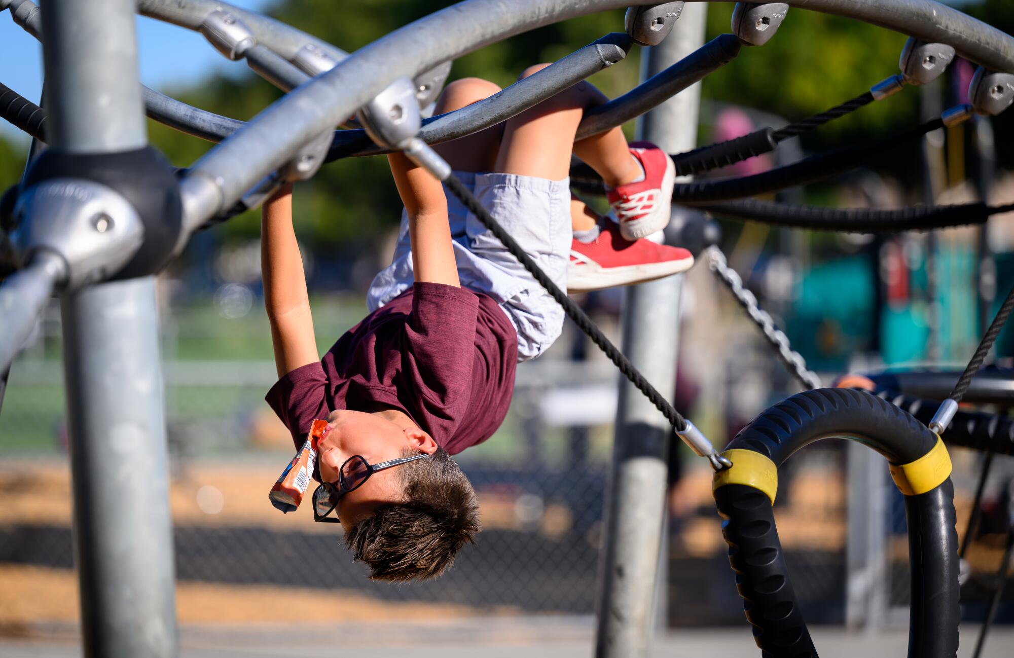 A boy hangs upside down on playground equipment. 