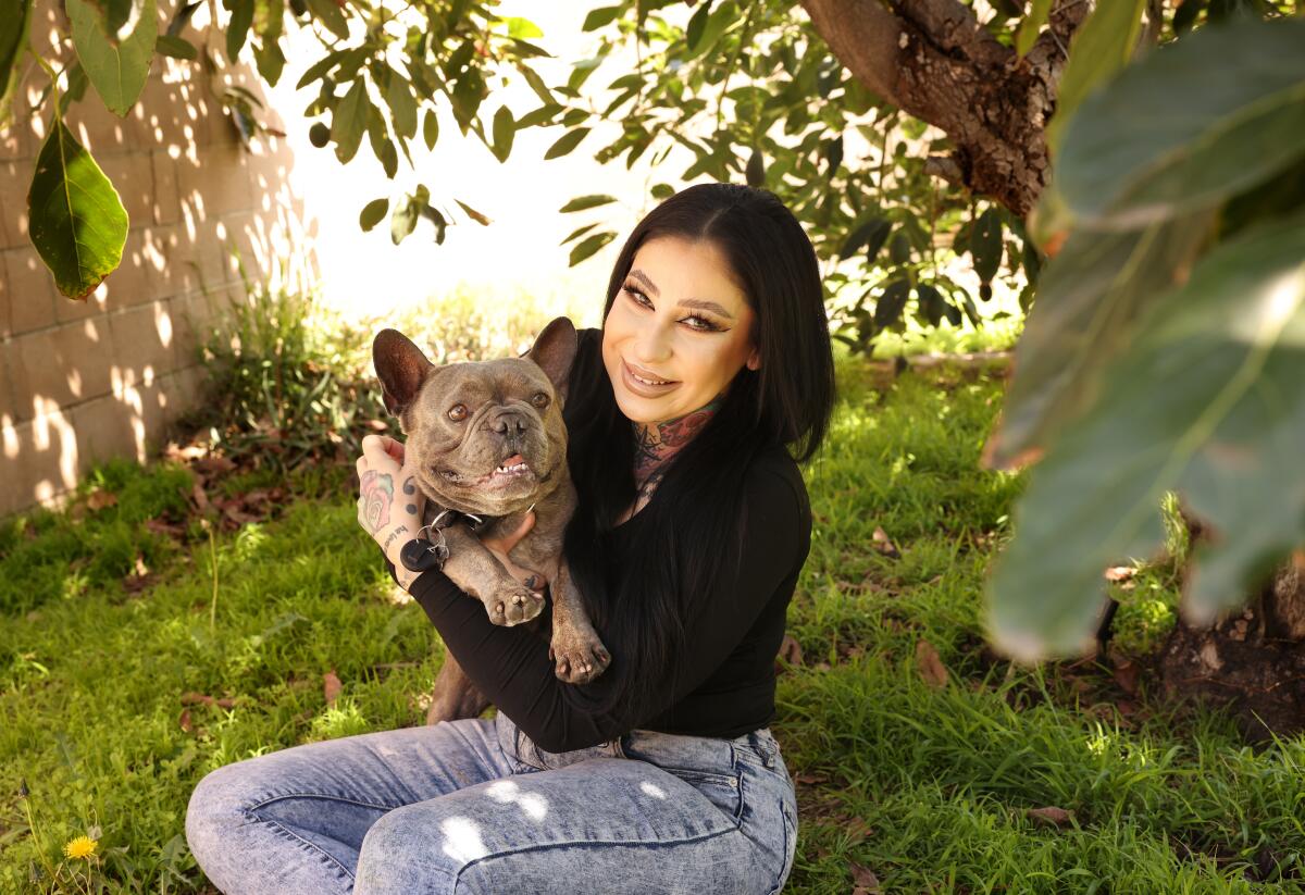 Yasmine Hazeart and her French bulldog named Havoc sit on grass under a tree.