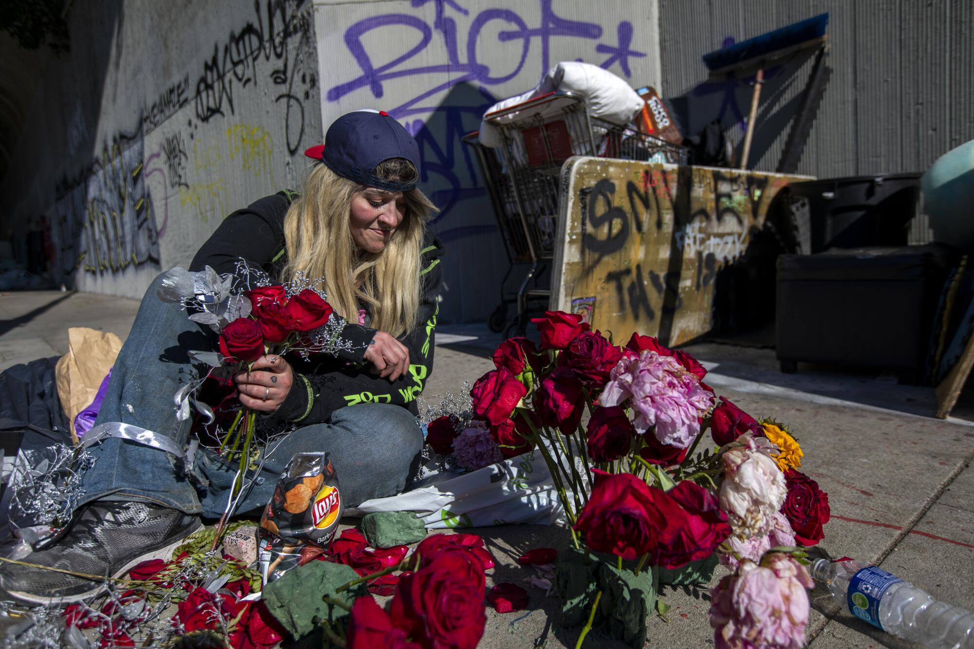 A woman sits while arranging flowers on a sidewalk. 