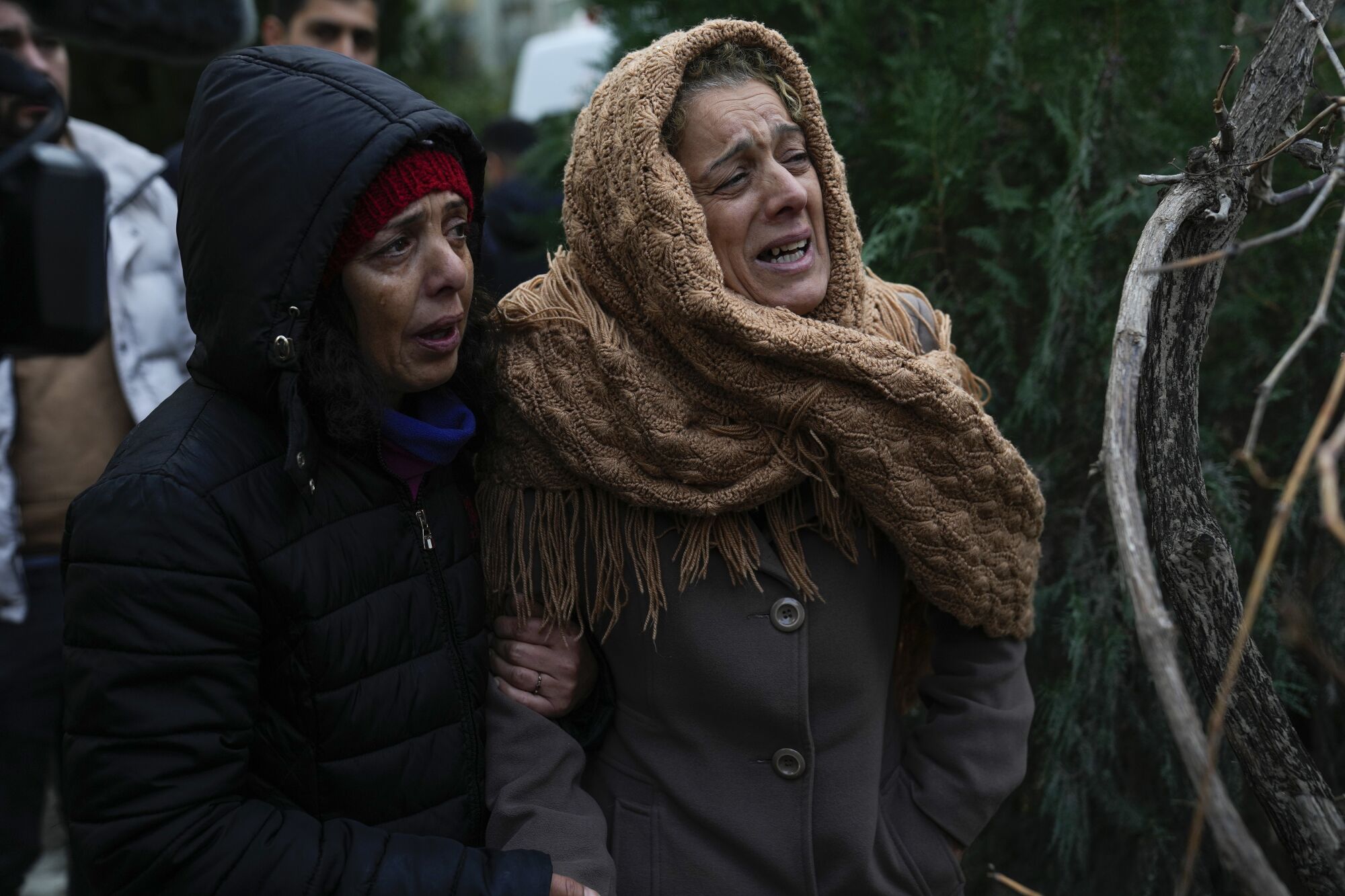 Adana'da acil durum ekipleri yıkılan bir binanın enkazında insanları ararken kadınlar ağlayarak izliyor.
