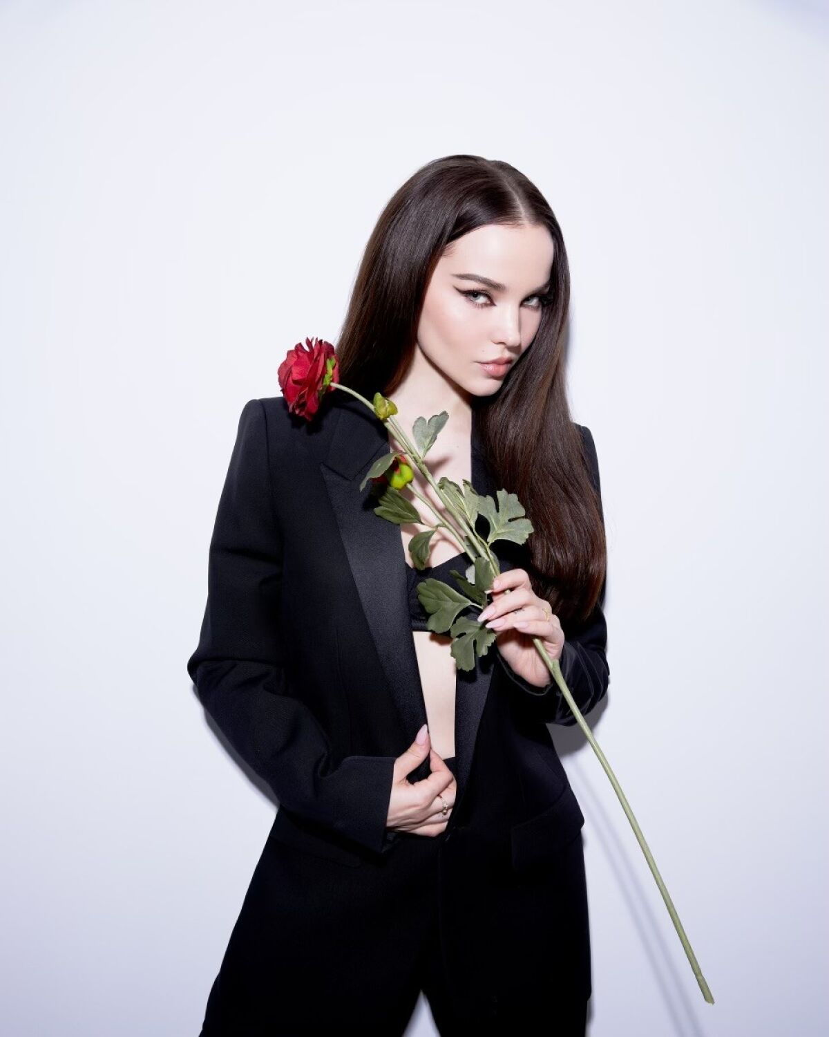 A woman in a black tuxedo holds a long-stemmed red rose