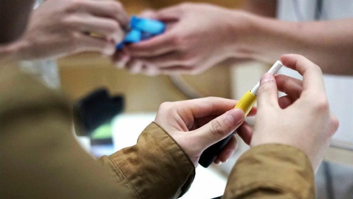 FILE - In this Oct. 22, 2018 file photo, visitors try out a pen-like "heat-not-burn" device at an IQOS store at Ginza in Tokyo. On Tuesday, April 30, 2019, the U.S. Food and Drug Administration said it will allow Philip Morris International to sell the cigarette alternative that heats tobacco without burning it. (AP Photo/Eugene Hoshiko)