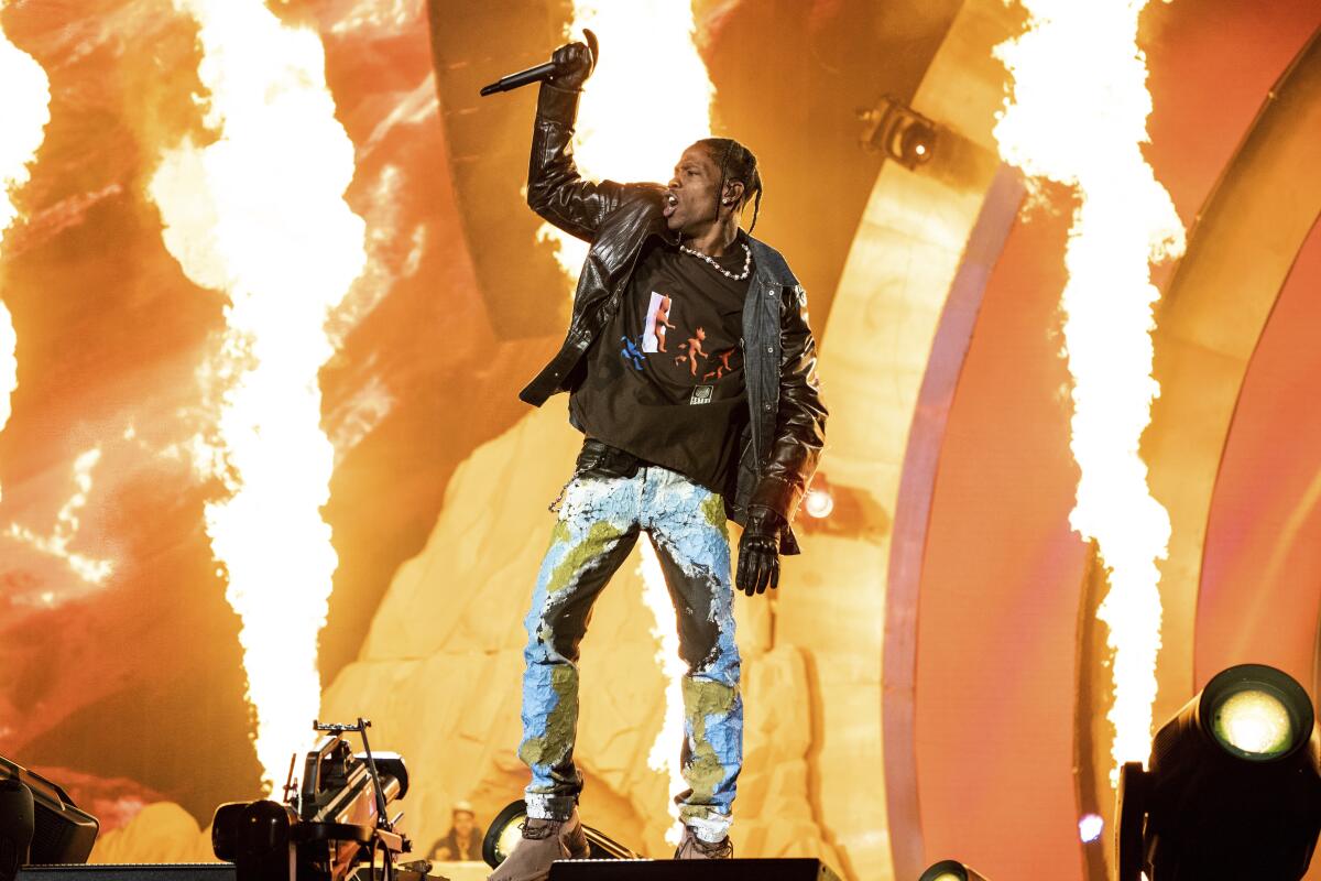 Travis Scott performs onstage with flames behind him.