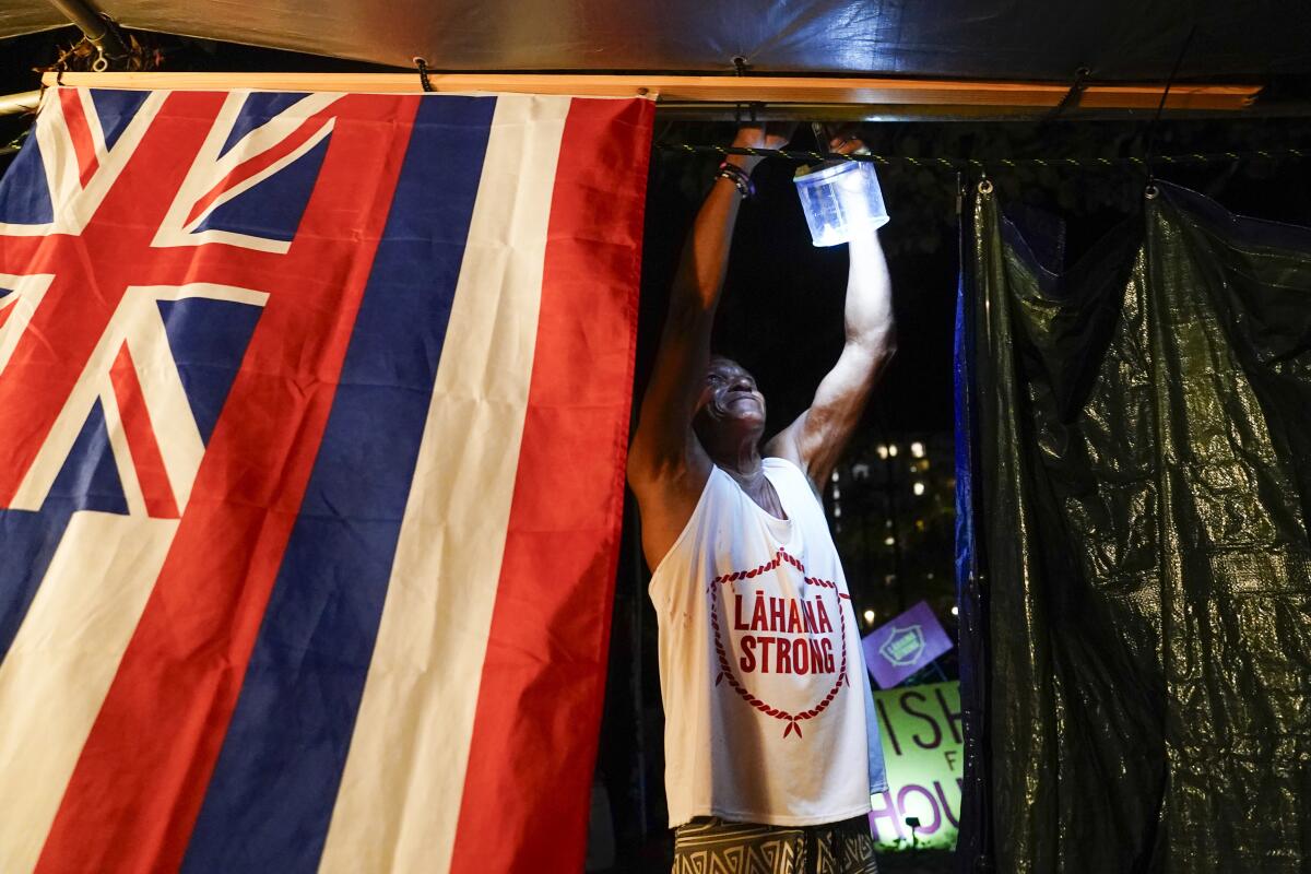 A man hangs up a light near a Hawaii state flag. 