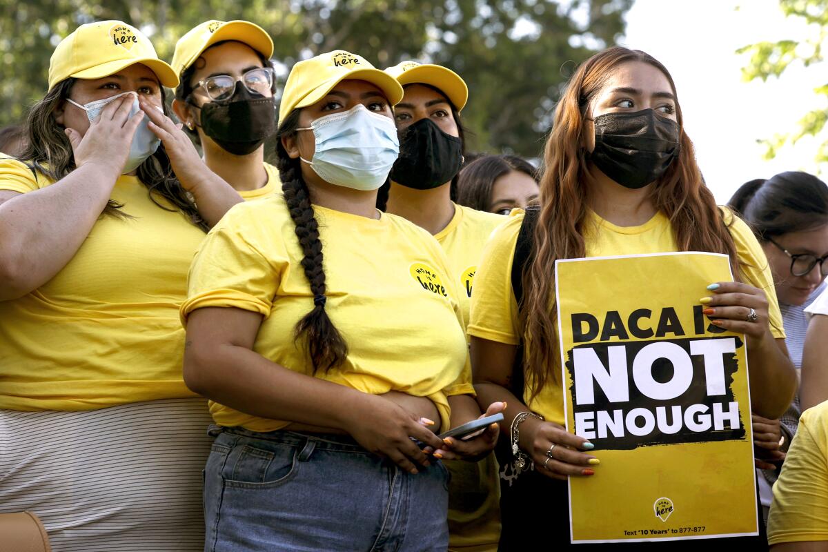 A group of people in yellow shirts and hats with a sign reading "DACA is not enough"