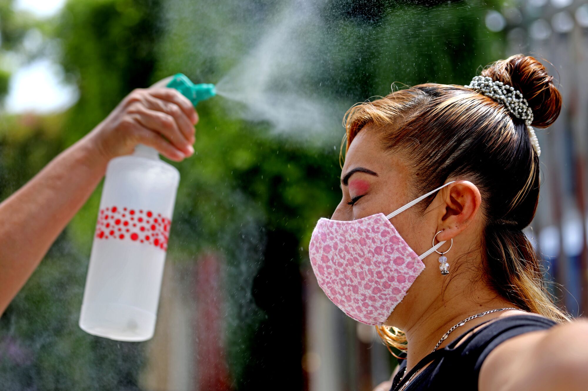 Mist from a spray bottle falls over a woman in a mask