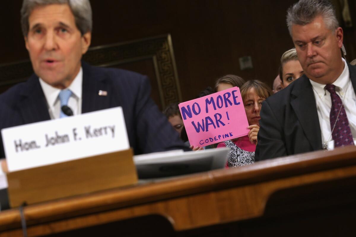 An antiwar protester holds a sign behind Secretary of State John F. Kerry as he testifies before the Senate Foreign Relations Committee. He is seeking congressional authorization for use of military force against Islamic State.