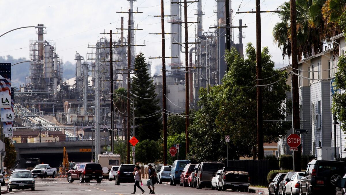 Pedestrians cross the street in a neighborhood near an oil refinery in the Wilmington area of Los Angeles.